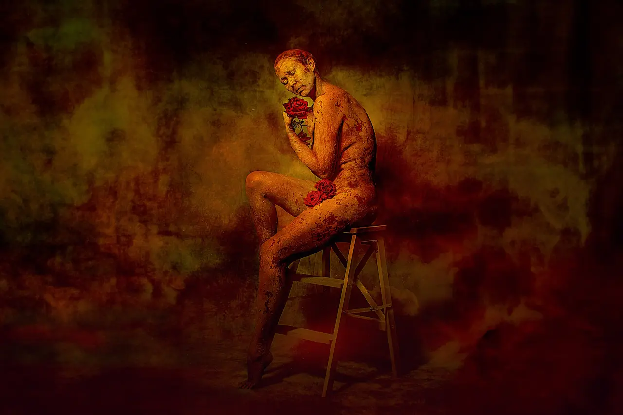 A woman seated on a stool, embracing herself while holding red roses close to her heart. Her body is covered in earthy textures, blending into the warm backdrop, symbolizing self-acceptance, love, and the beauty of embracing one's own journey of transformation and inner strength