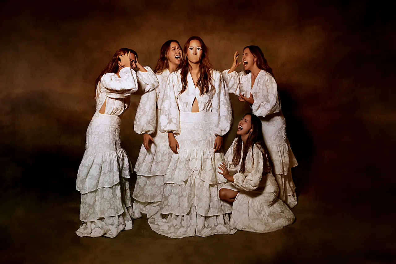 A woman stands silent in the center with no mouth, while multiple versions of herself around her express emotions and speak out, symbolizing the feeling of being voiceless as others have a say. She wears a flowing white gown, set against a deep brown backdrop, capturing the struggle of being unheard