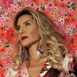 A vibrant portrait of a woman wearing a flowing floral dress, set against a matching floral background. Captured by Jussara Valente Photography, this artistic image showcases elegance, boldness, and a celebration of feminine beauty and expression.